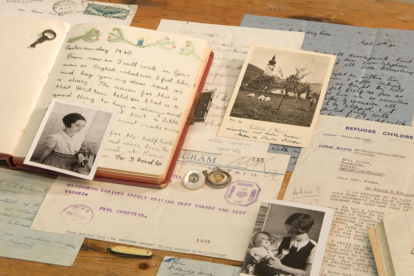 Several historical documents layered on top of each other, including an open diary, a photograph of a house in the country, telegram, and other typewritten papers.