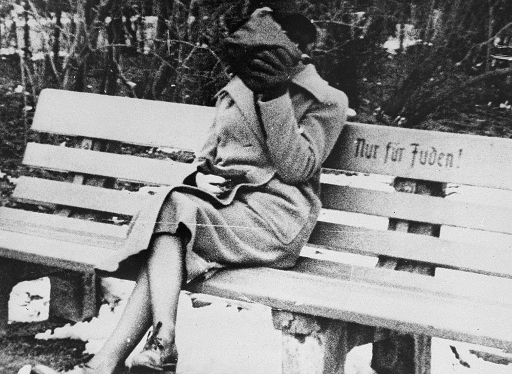 A woman sits on a park bench marked “Only for Jews.” Austria, ca. March 1938.