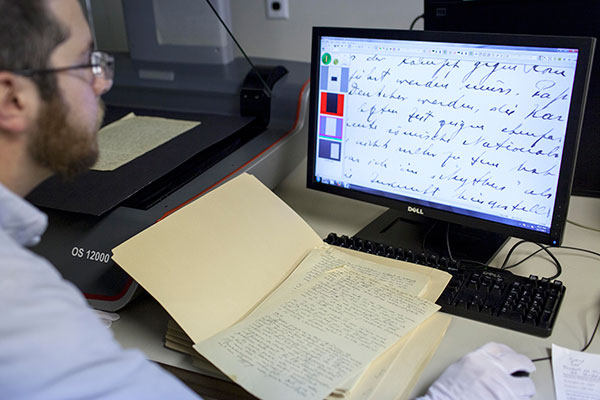 A museum employee sits at a computer, with a copy of a document up on his screen