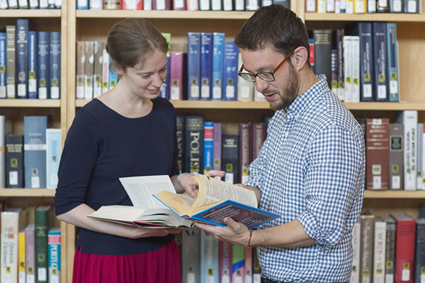 Two people stand and read from a book in the Museum Library