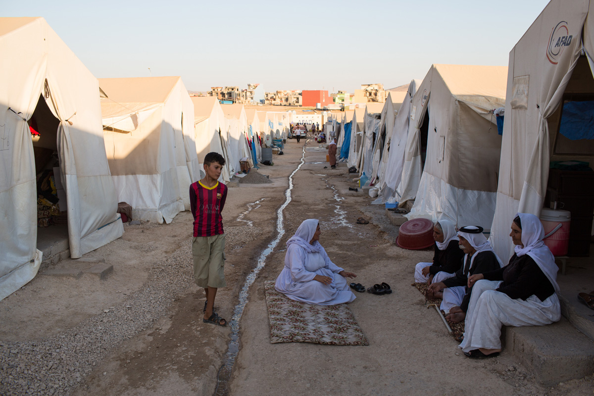 People walk and sit between a row of tents.