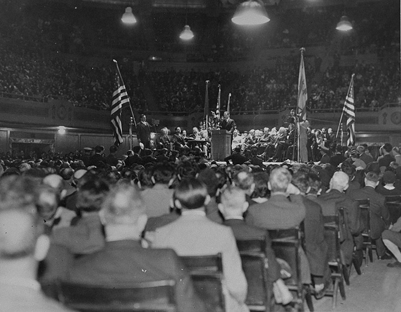 A man stands at a podium surrounded by crowds