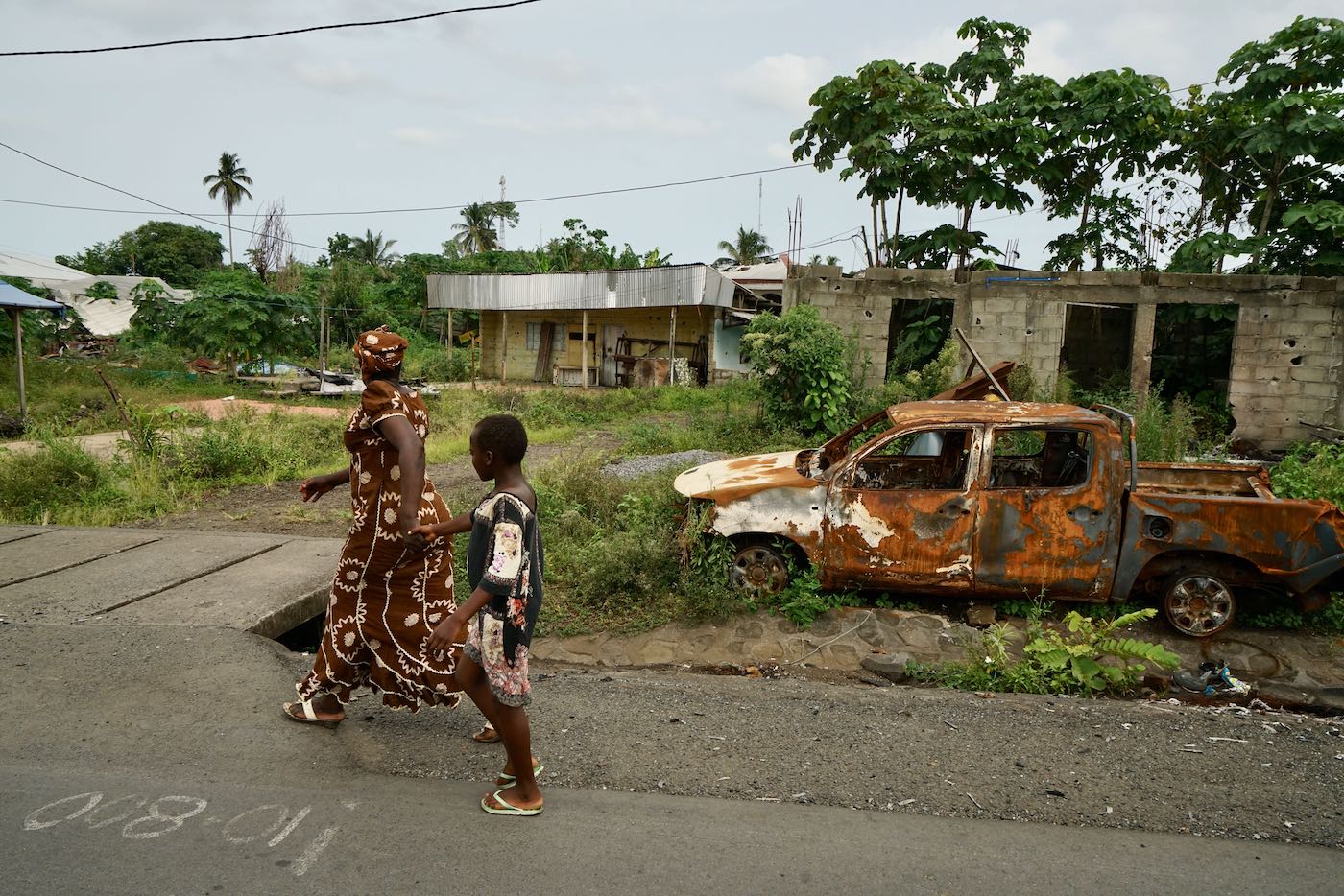 May 11, 2019: A mother and child walk past a destroyed car in a small town on the main highway near Buea in Southwest Cameroon.