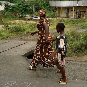 May 11, 2019: A mother and child walk past a destroyed car in a small town on the main highway near Buea in Southwest Cameroon.