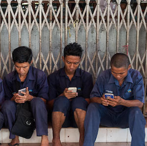 Workers sit in front of a Buddhist temple during their break and use their smartphones. January 27, 2017, Yangon, Republic of the Union of Myanmar, Asia.