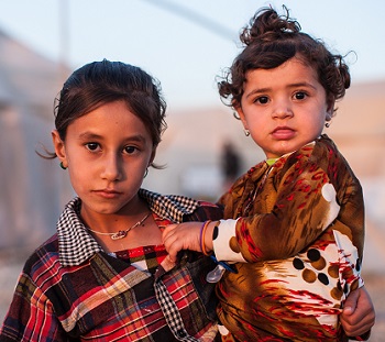 A young Yezidi girl carries her sister in a displaced persons camp in Dohuk, Iraq.