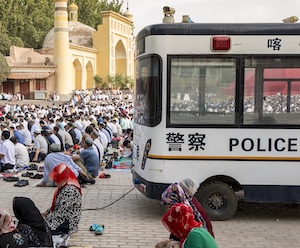 In July 2015, outside the Id Kah Mosque in the ancient Silk Road trade town of Kashgar, Uyghur men and women pray during Eid al-Fitr, a joyous Muslim holiday that marks the end of Ramadan. Police vehicles and security line the public square in Xinjiang, China.